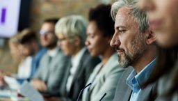A row of professionals sitting at a conference table with one man in focus