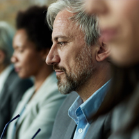 A row of professionals sitting at a conference table with one man in focus