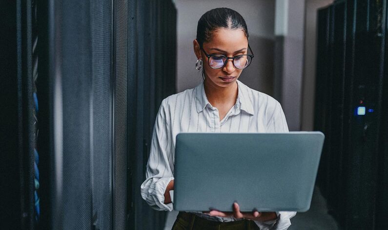 Shot of a young woman using a laptop while working in a server room