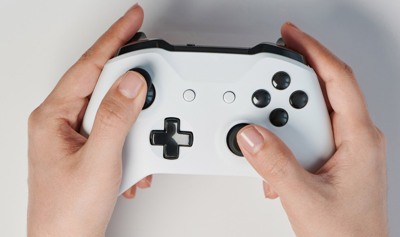 Close-up of hands holding a white gaming controller with black buttons, highlighting the thumbsticks and D-pad.